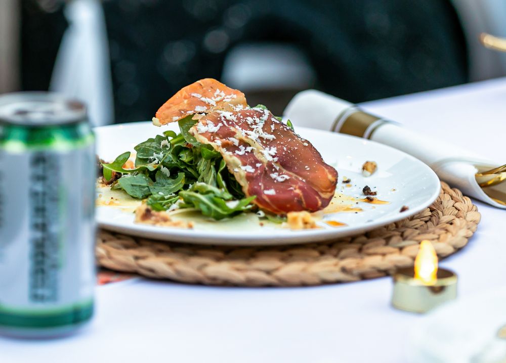 Elegant plated salmon dish with prosciutto and fresh greens on a woven placemat with a candle.