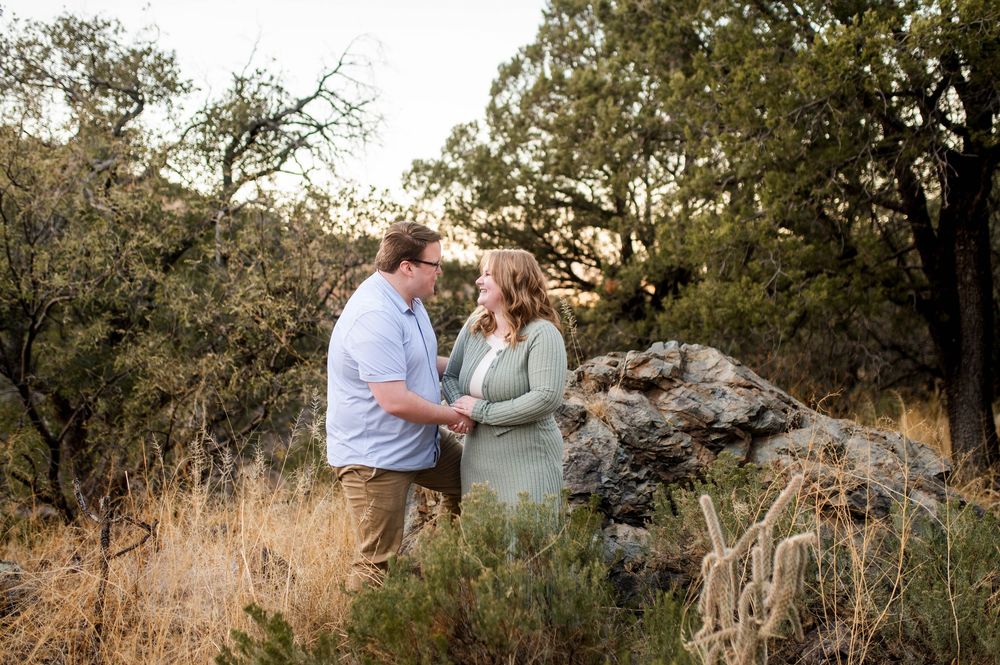 Couple holding hands and gazing at each other in golden desert landscape at sunset.