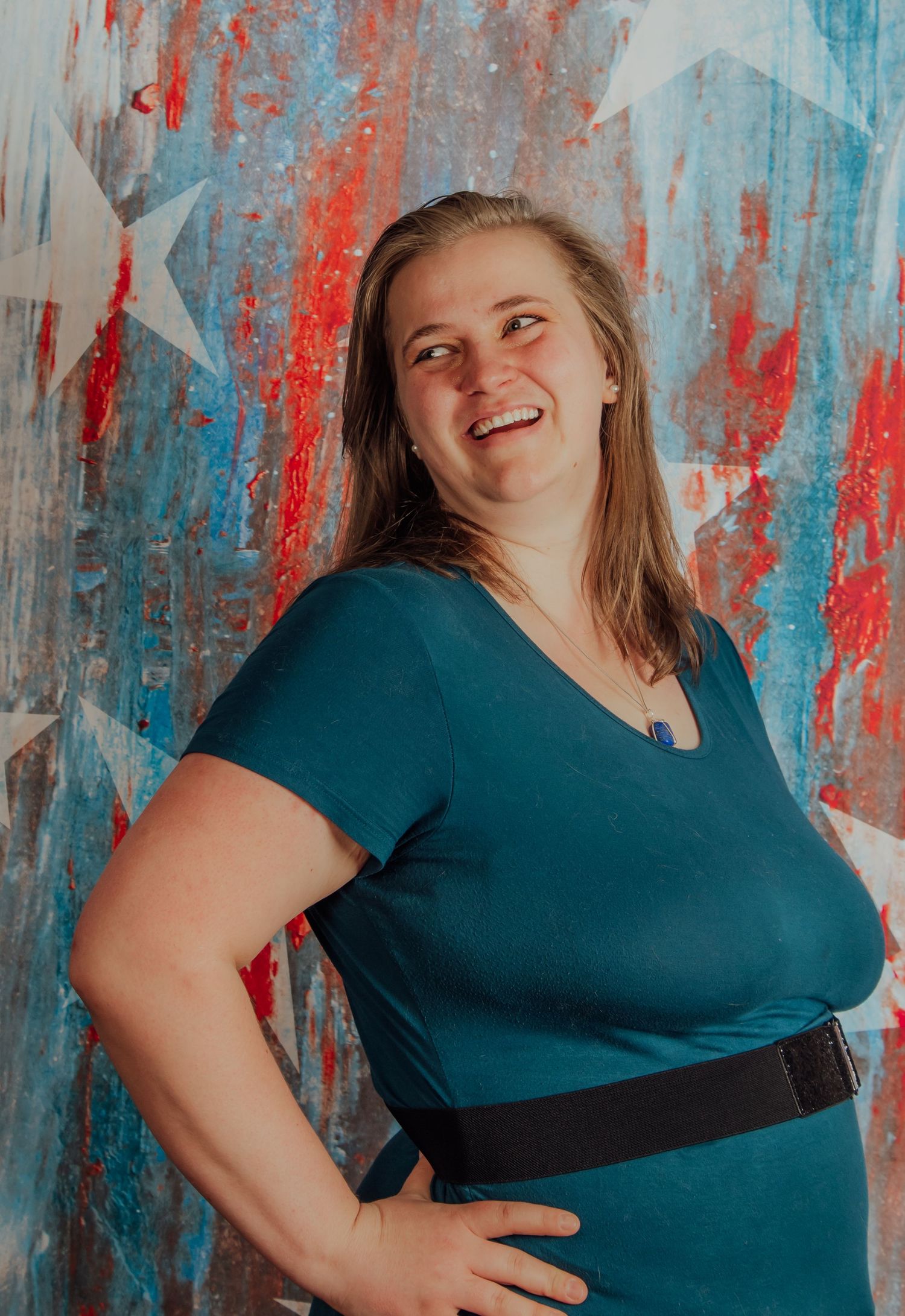 Smiling woman in teal dress poses against patriotic red, white, and blue star-painted backdrop.