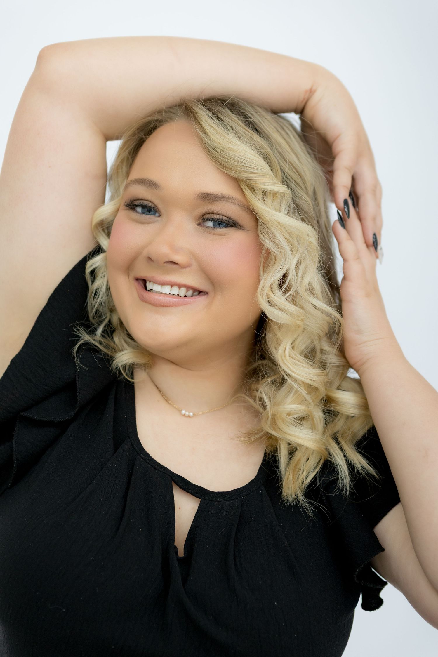 Smiling blonde woman in black ruffled top posing confidently against a white background.