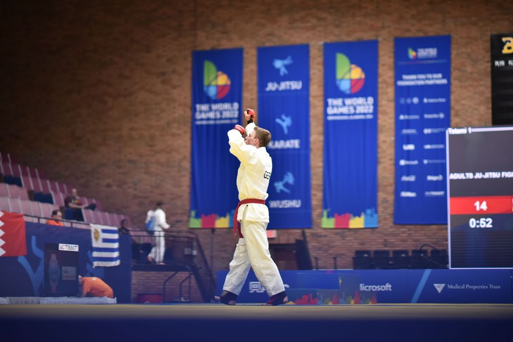 Judo athlete in white gi celebrates victory at The World Games 2022 ju-jitsu competition in indoor arena.