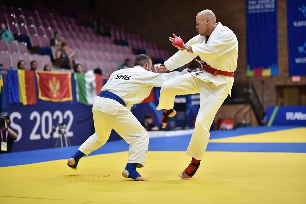 Two judo athletes compete on a mat at the 2022 World Games, one executing a high kick during an intense match.
