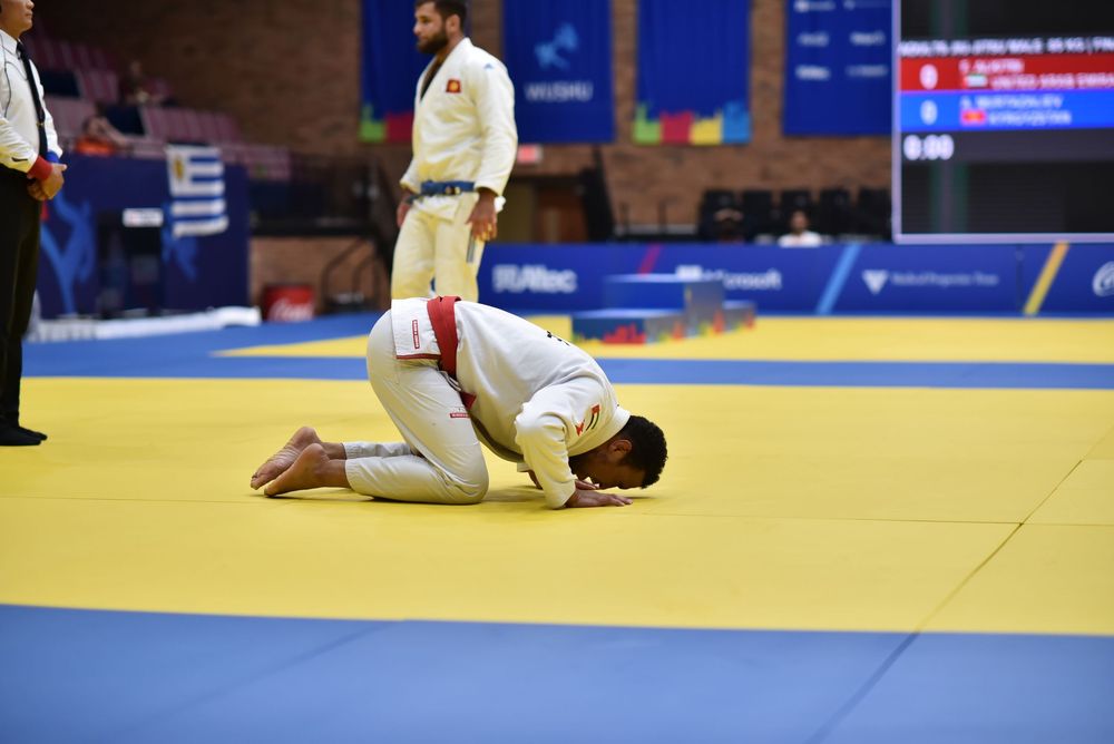 Two judo athletes compete on a yellow mat during an official judo tournament match in a sports arena.