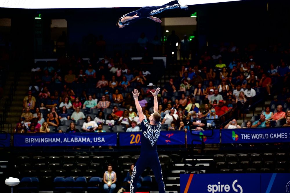 Volleyball player serves ball at The World Games in Birmingham, Alabama, USA, with crowd in background.