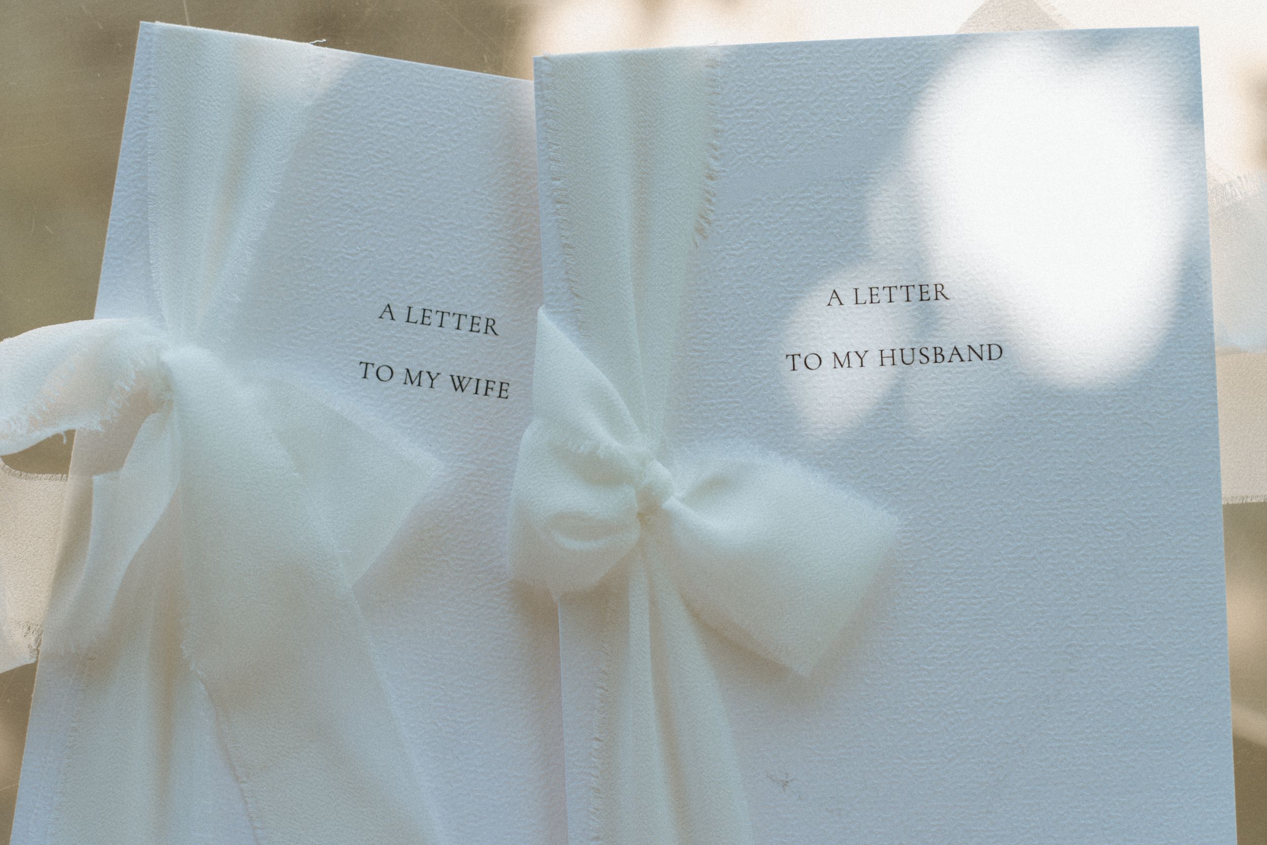 Two white wedding vow books tied with sheer ribbon, labeled A Letter To My Wife and A Letter To My Husband.