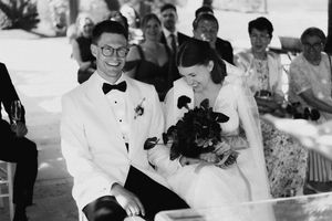 Black and white photo of a smiling bride and groom sitting together during their outdoor wedding ceremony.