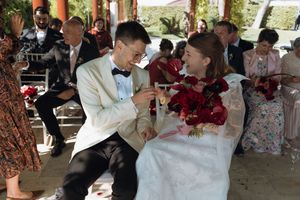 Bride and groom laughing together during outdoor wedding ceremony, sharing champagne toast under decorative pavilion.