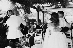 Black and white photo of wedding couple sharing first kiss at outdoor ceremony with guests seated in white chairs.