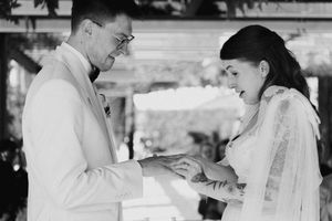 Black and white photo of a groom placing a wedding ring on his bride's finger during a ceremony.