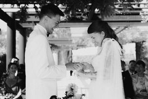 Black and white photo of bride and groom exchanging rings during elegant outdoor wedding ceremony.