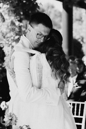 Black and white photo of bride and groom sharing a tender embrace during their outdoor wedding ceremony.