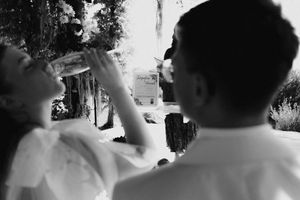 Black and white photo of a couple outdoors, woman drinking from a bottle, man in white shirt beside her.
