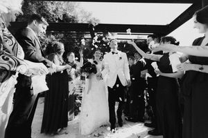 Black and white wedding photo of bride and groom walking through cheering guests throwing confetti.