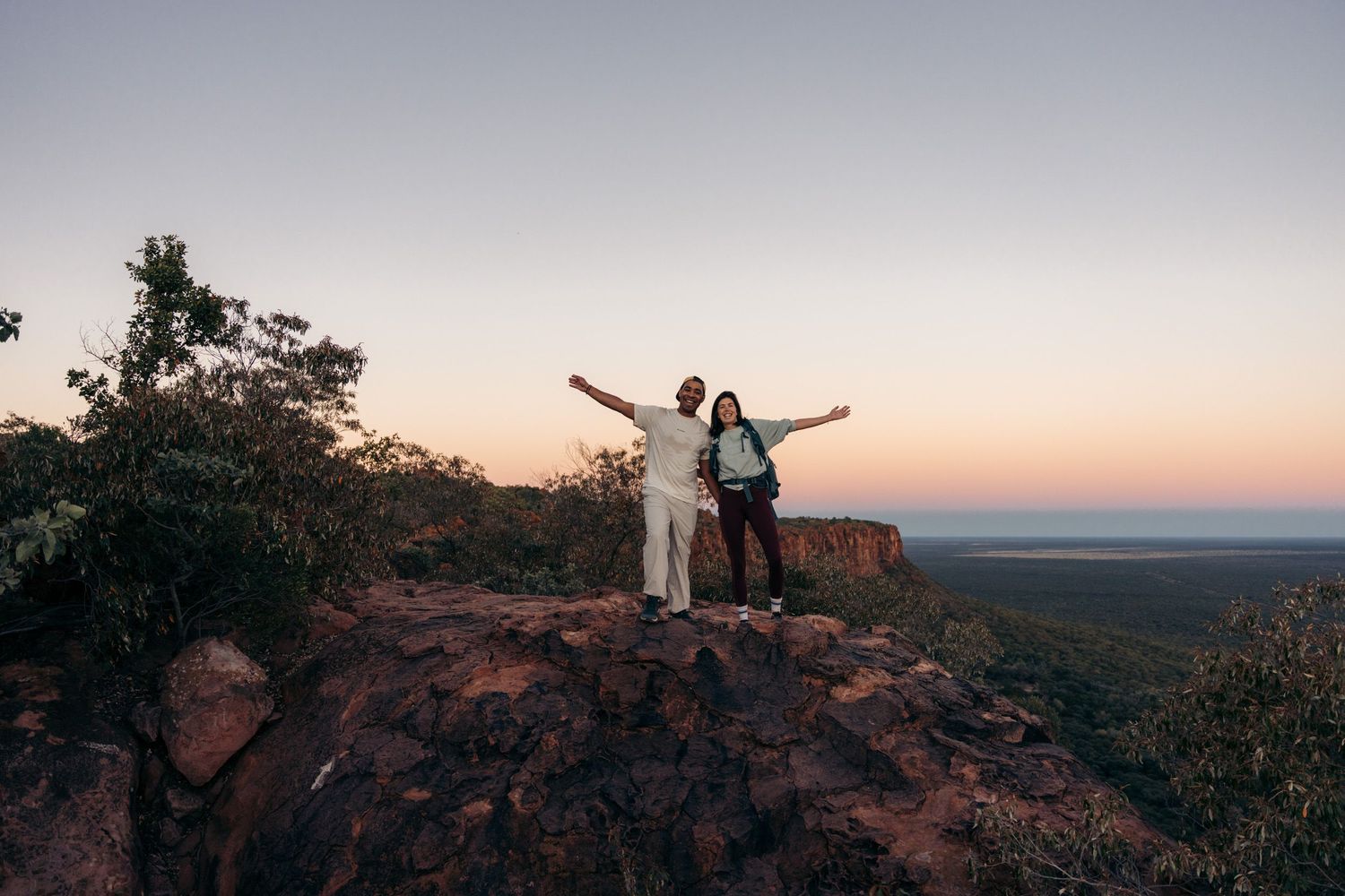 couple qui lève les bras au sommet d'une falaise rouge qui domines d'immenses plaines du plateau de waterberg au coucher du soleil