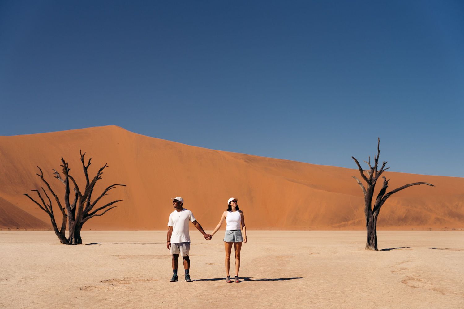 couple à deadvlei qui se tient la main au milieu des accacias noirs du désert avec les dunes rouges en arrière-plan