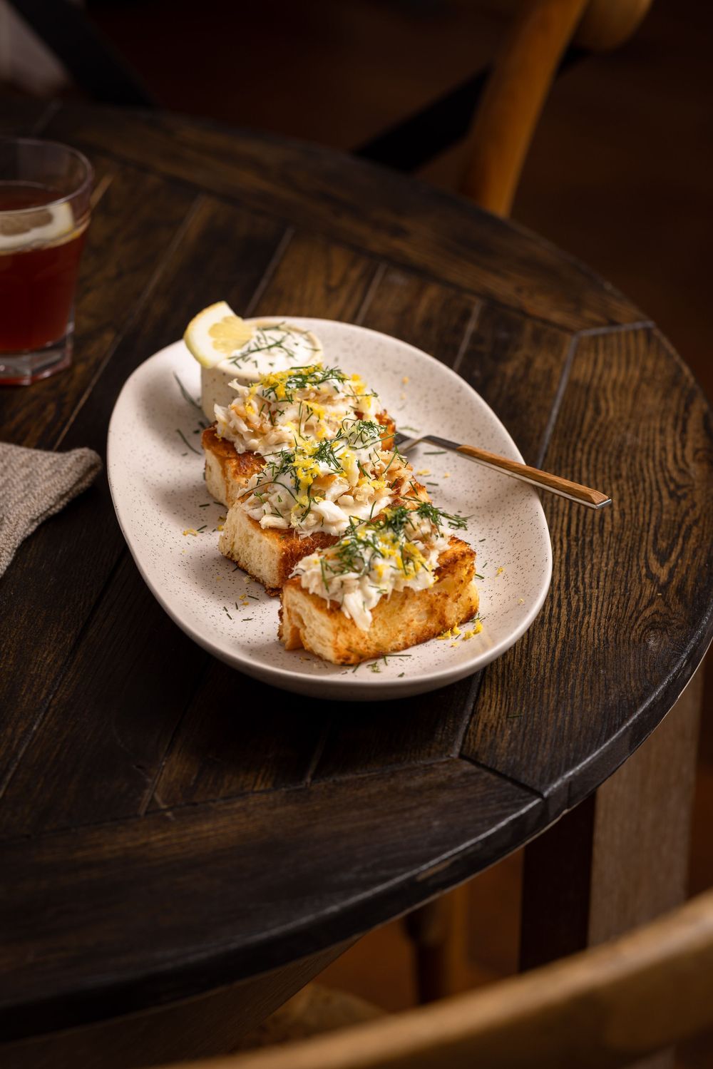 Golden toasted bread topped with creamy sauce, fresh herbs, and lemon on a rustic wooden table.