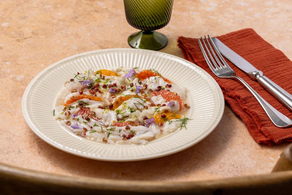 Elegant risotto dish garnished with fresh herbs, edible flowers, and seafood, served on a white plate with silverware.