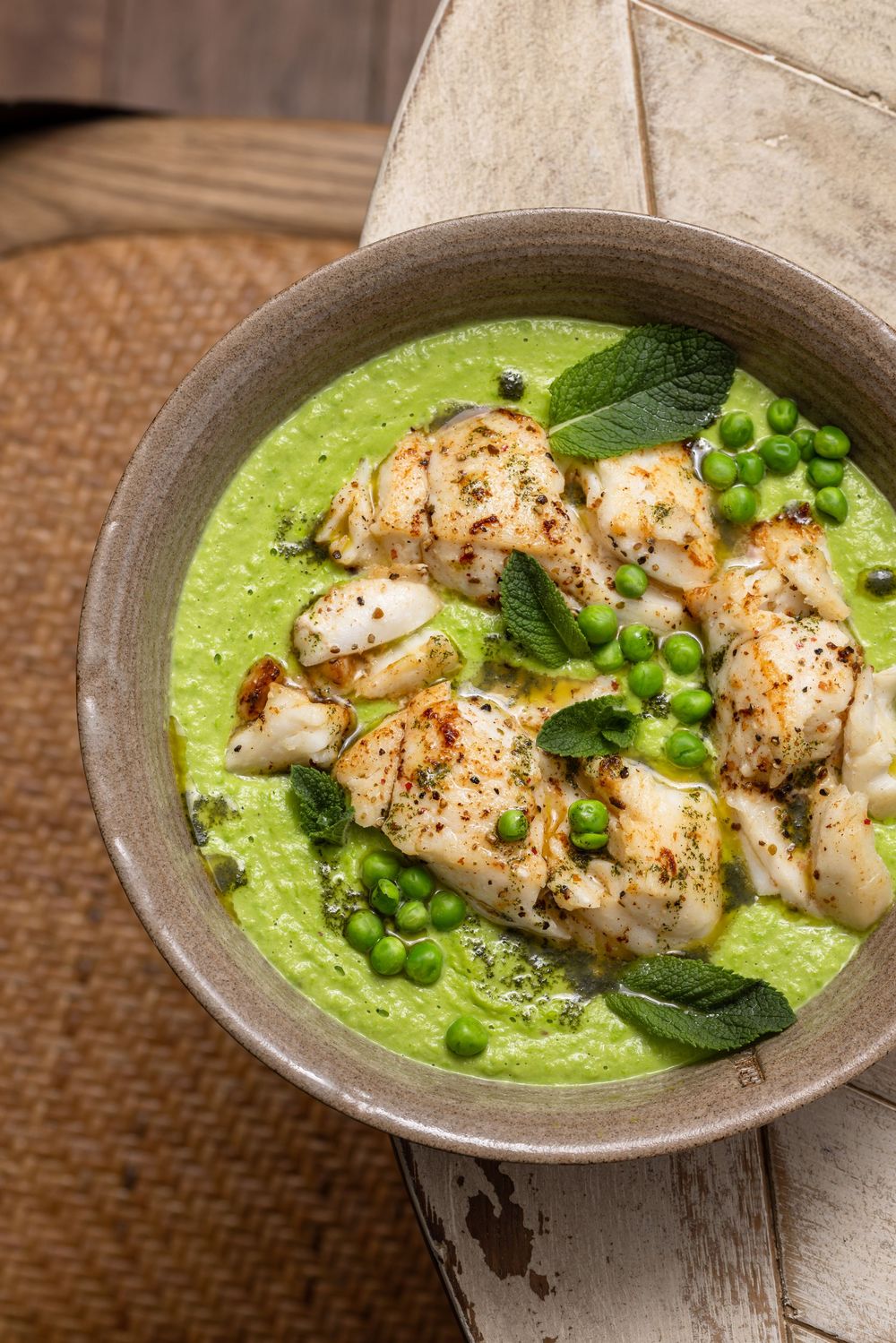 Grilled shrimp served over creamy green pea soup garnished with fresh peas and sage leaves in a rustic bowl.
