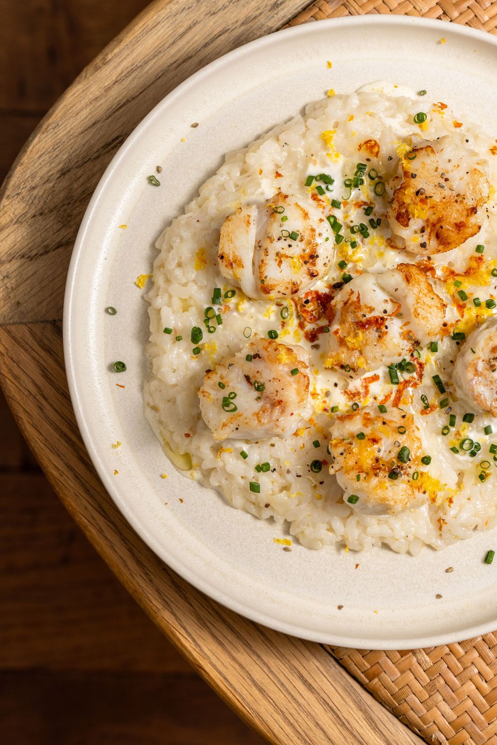 Overhead view of creamy shrimp and grits topped with seasoned shrimp, chives, and spices on a white plate.