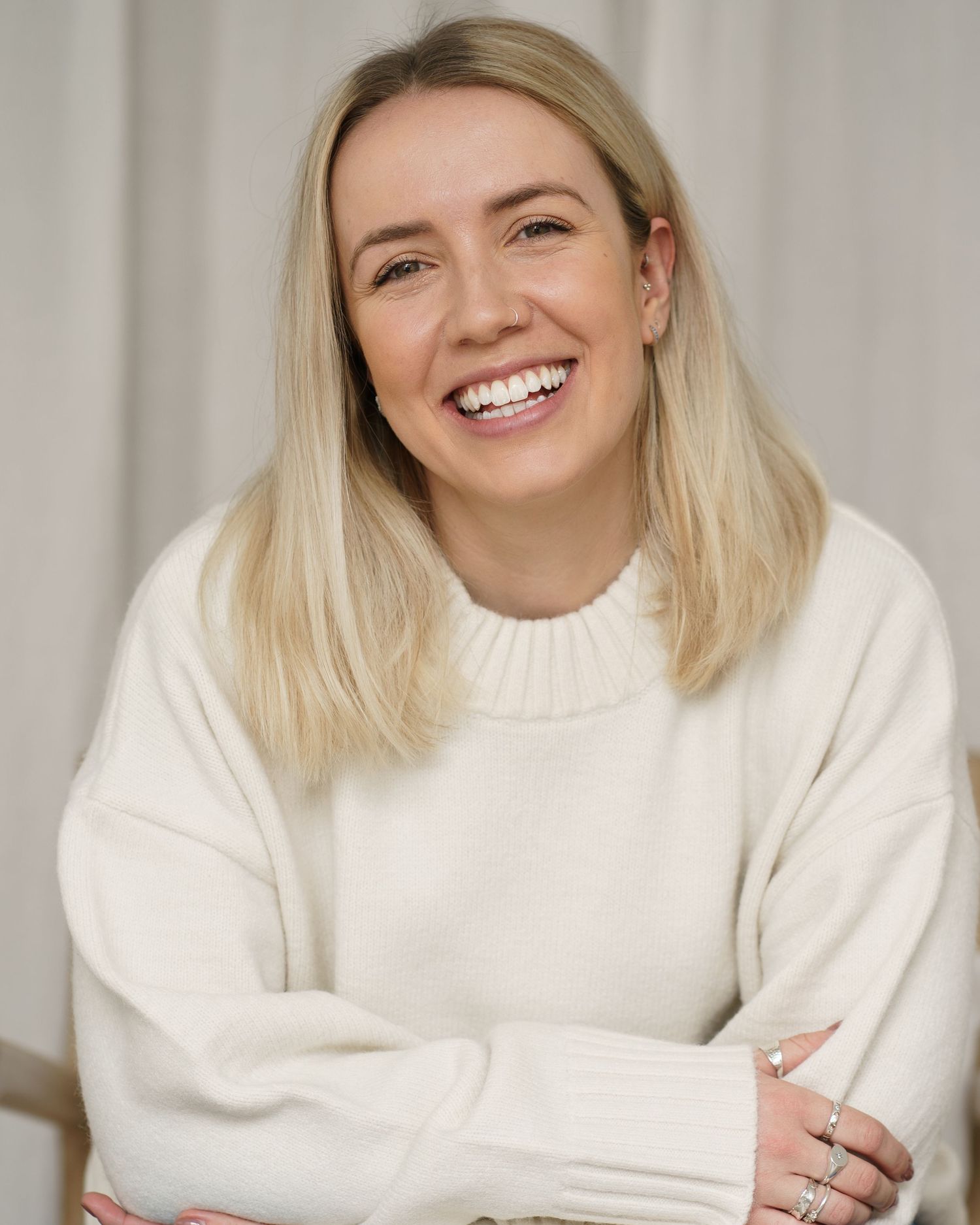 Smiling blonde woman in a white sweater with arms crossed, posing for a professional portrait photo.