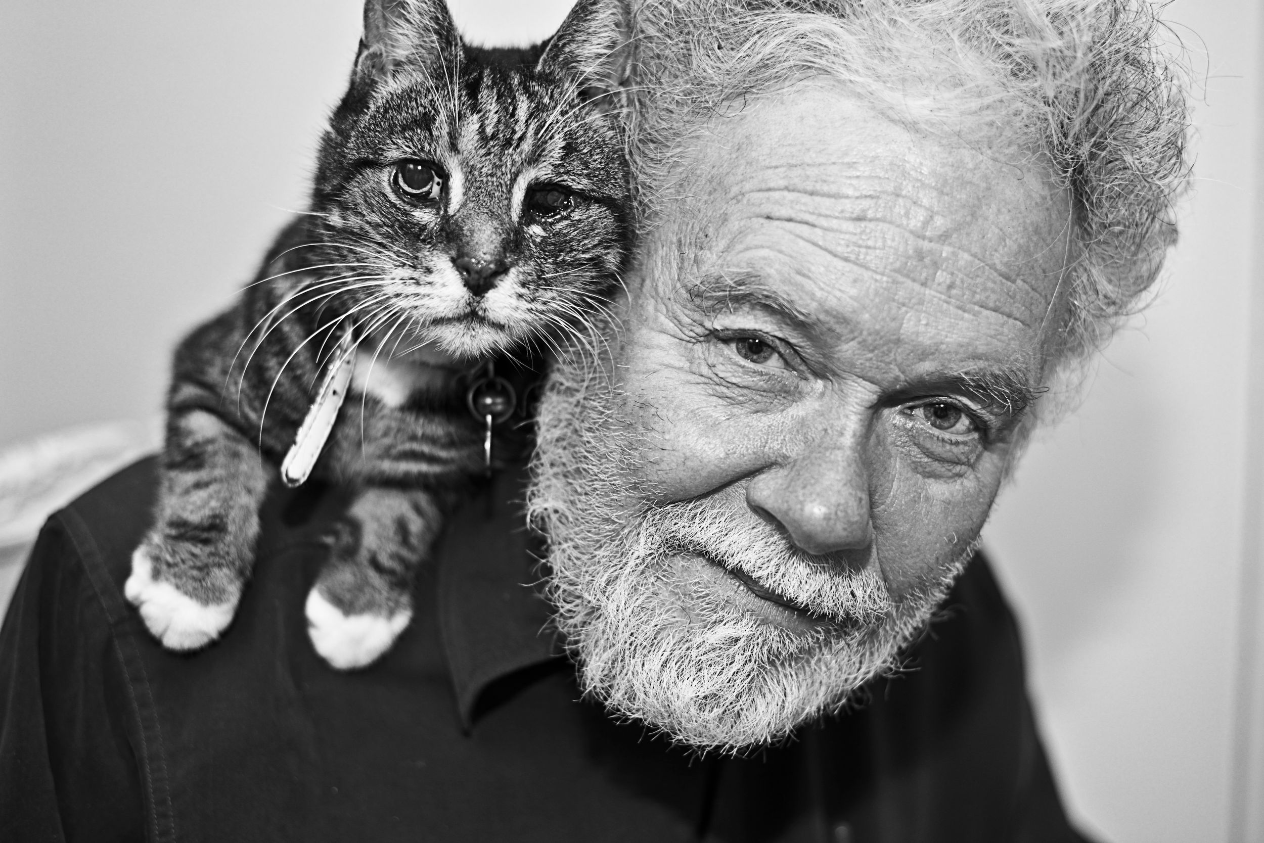 Black and white portraits of an elderly person with cats resting on their shoulders.