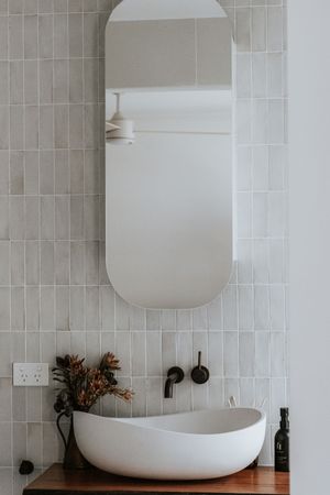 Modern bathroom with oval mirror, white vessel sink on wood vanity, matte black faucet, and grey subway tiles.