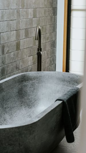 A modern concrete freestanding bathtub with a sleek black faucet against gray subway tiles in a minimalist bathroom.