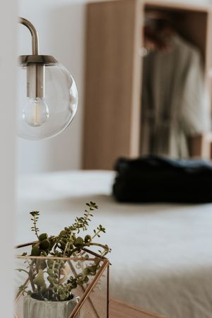 Modern bedroom with globe wall sconce, copper geometric plant holder with succulents, and blurred wardrobe in background.