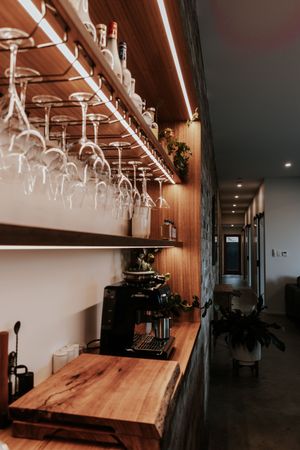 Modern bar shelf with hanging wine glasses, LED lighting, wooden countertop, and espresso machine in a stylish restaurant.