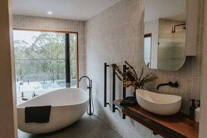 Modern bathroom with freestanding oval tub, wooden vanity, vessel sink, and large window overlooking lush greenery.