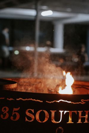 A fire pit with flames and smoke, labeled '35 South', glowing warmly against a dark outdoor background.