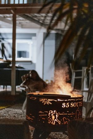 Decorative metal fire pit with cutout designs and '35 South' text, glowing with warm flames outdoors at night.