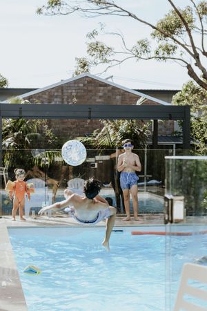 Children playing with a beach ball in a backyard swimming pool on a sunny day.