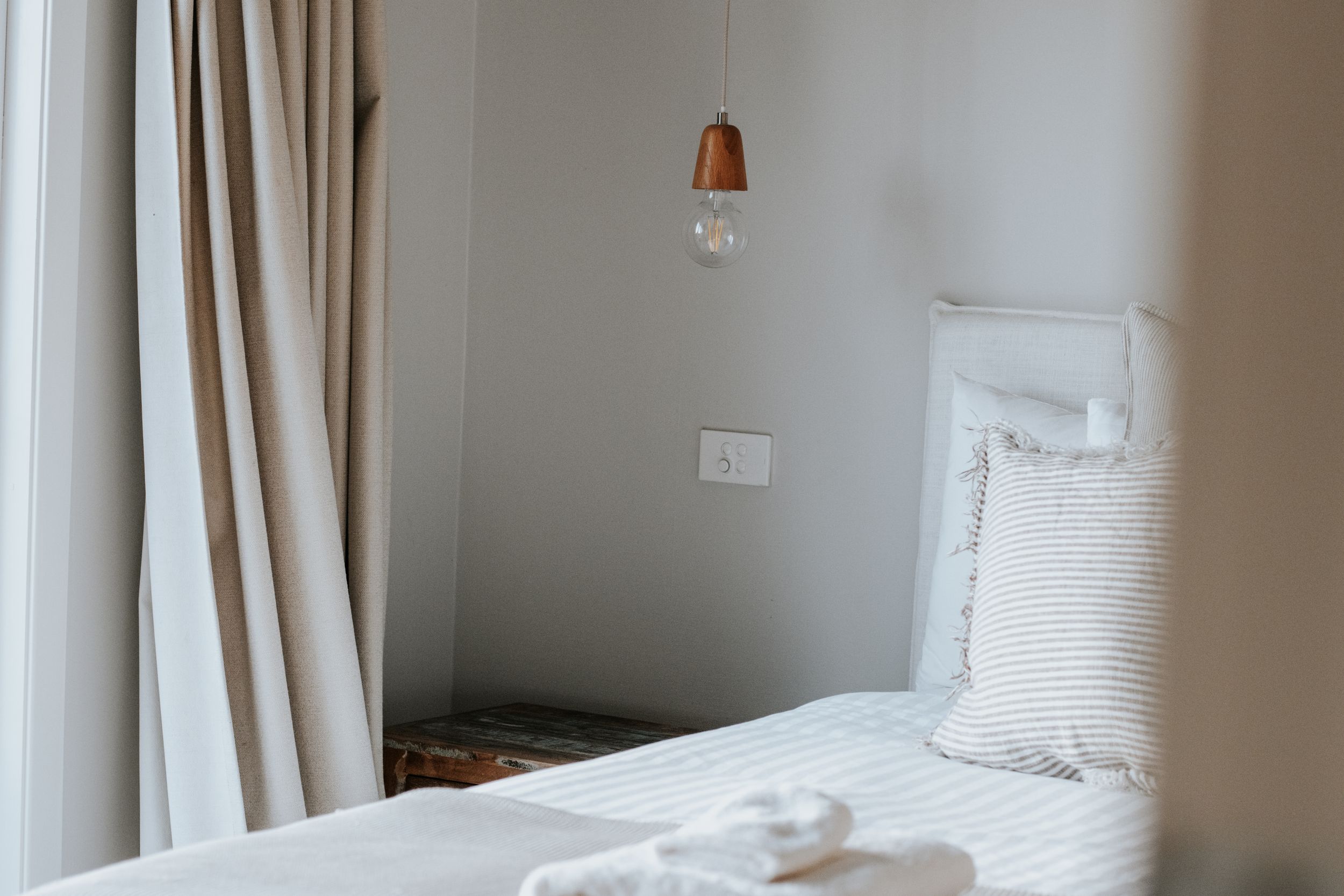 Minimalist white bedroom with striped pillows, pendant light, and neutral curtains for a serene retreat.