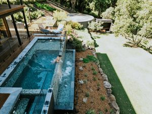 Aerial view of a modern infinity pool with water feature, surrounded by lush greenery and manicured lawn.