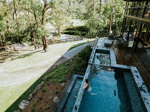 Aerial view of a luxury pool surrounded by lush forest, with a person swimming in the serene outdoor retreat.