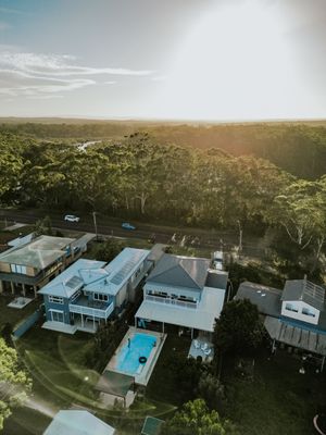 Aerial drone view of coastal Australian homes with pool surrounded by lush eucalyptus forest at golden sunset.