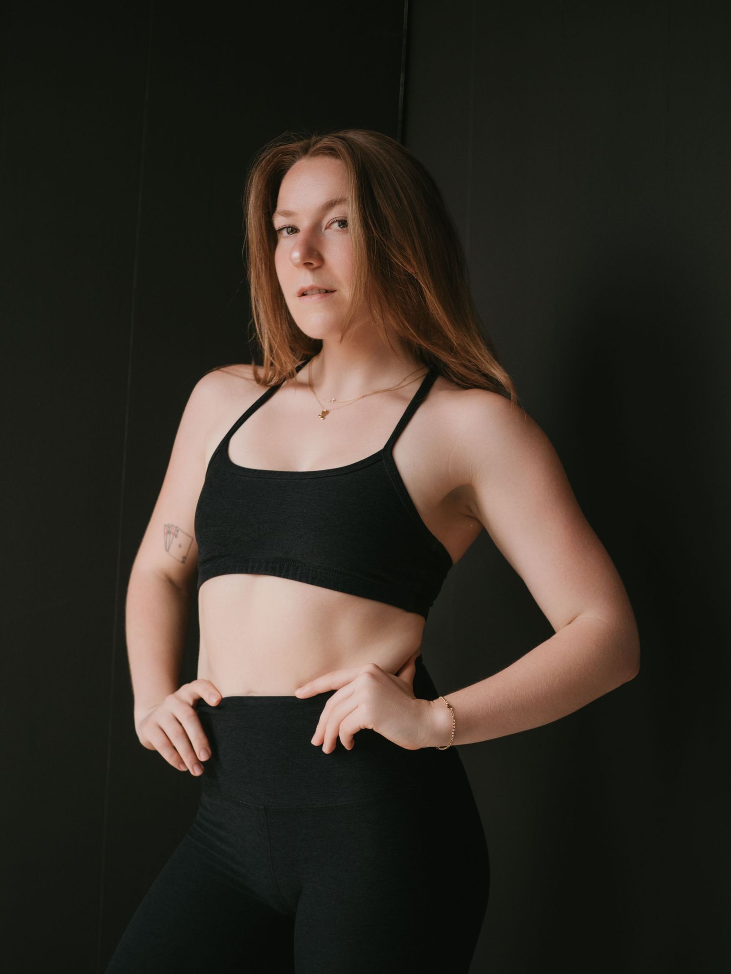 Black and white photo of a fit woman in athletic wear holding a volleyball, posing against a dark background.