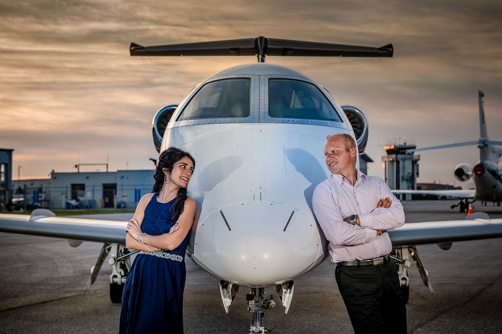 Couple standing back-to-back with arms crossed in front of a private jet at sunset on tarmac.
