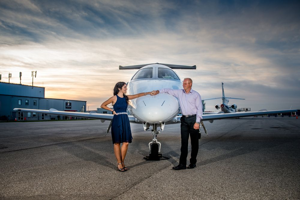 Woman in blue dress touching nose of private jet while man in suit stands beside her on tarmac.