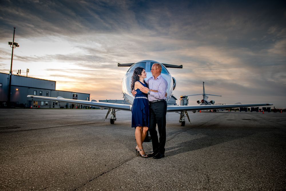 Romantic couple dancing and embracing on airport tarmac with private jet and colorful sunset sky.