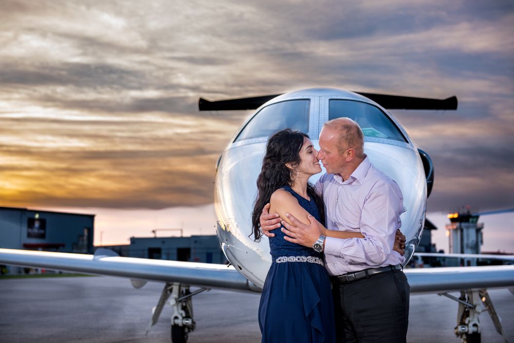 Couple sharing a romantic moment near the nose of a private jet under a vibrant sunset sky.