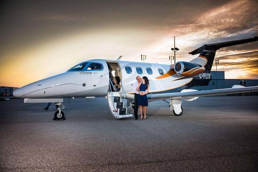 Couple kissing at the stairs of a private jet on airport tarmac during a stunning golden sunset.