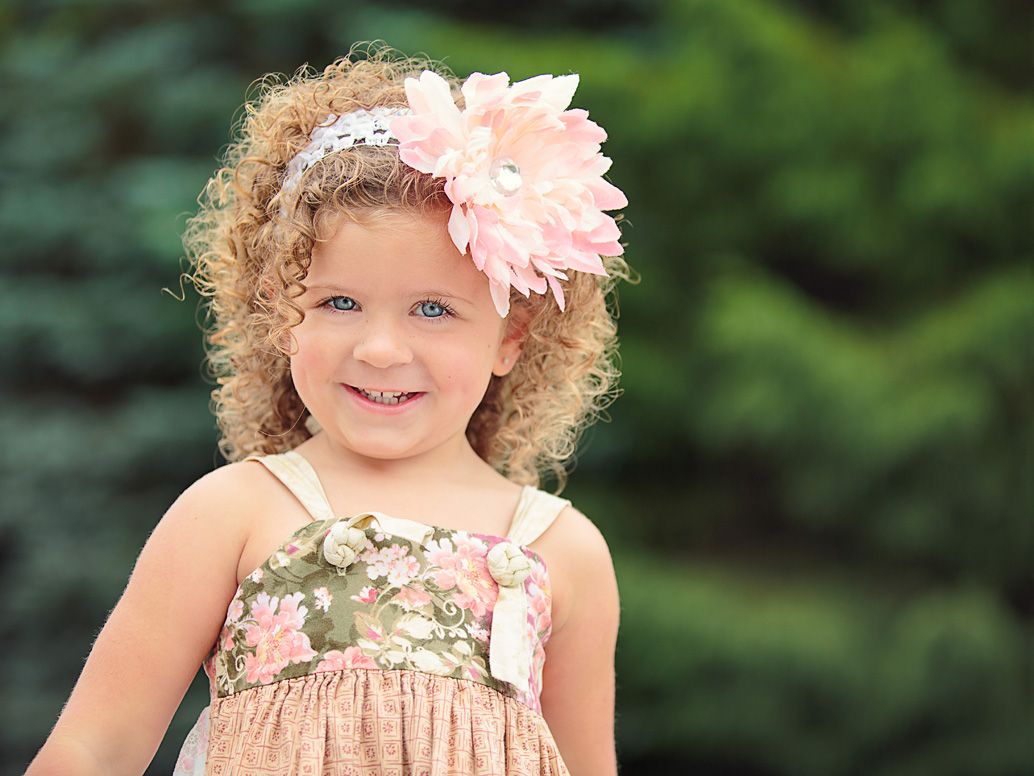 Smiling young girl with curly hair and floral pink headband at outdoor park by Brighton, MI family photographer