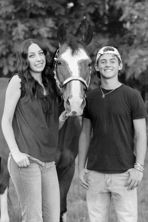 Black and white photo of a young couple smiling beside a horse outdoors.
