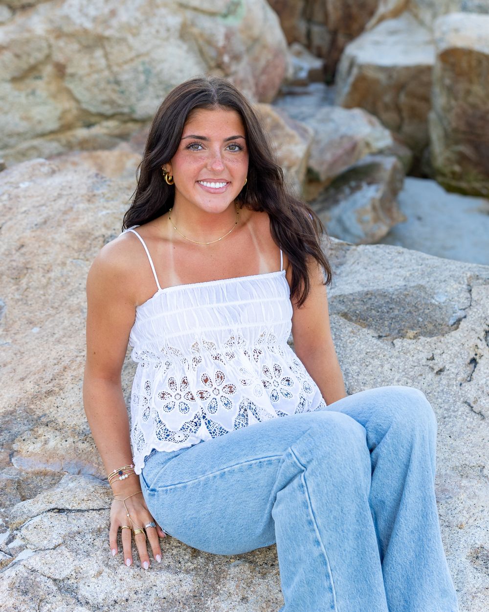 High school senior in poses on large rocks at Wingaersheek Beach in Gloucester, MA for yearbook portrait session at sunset golden hour.