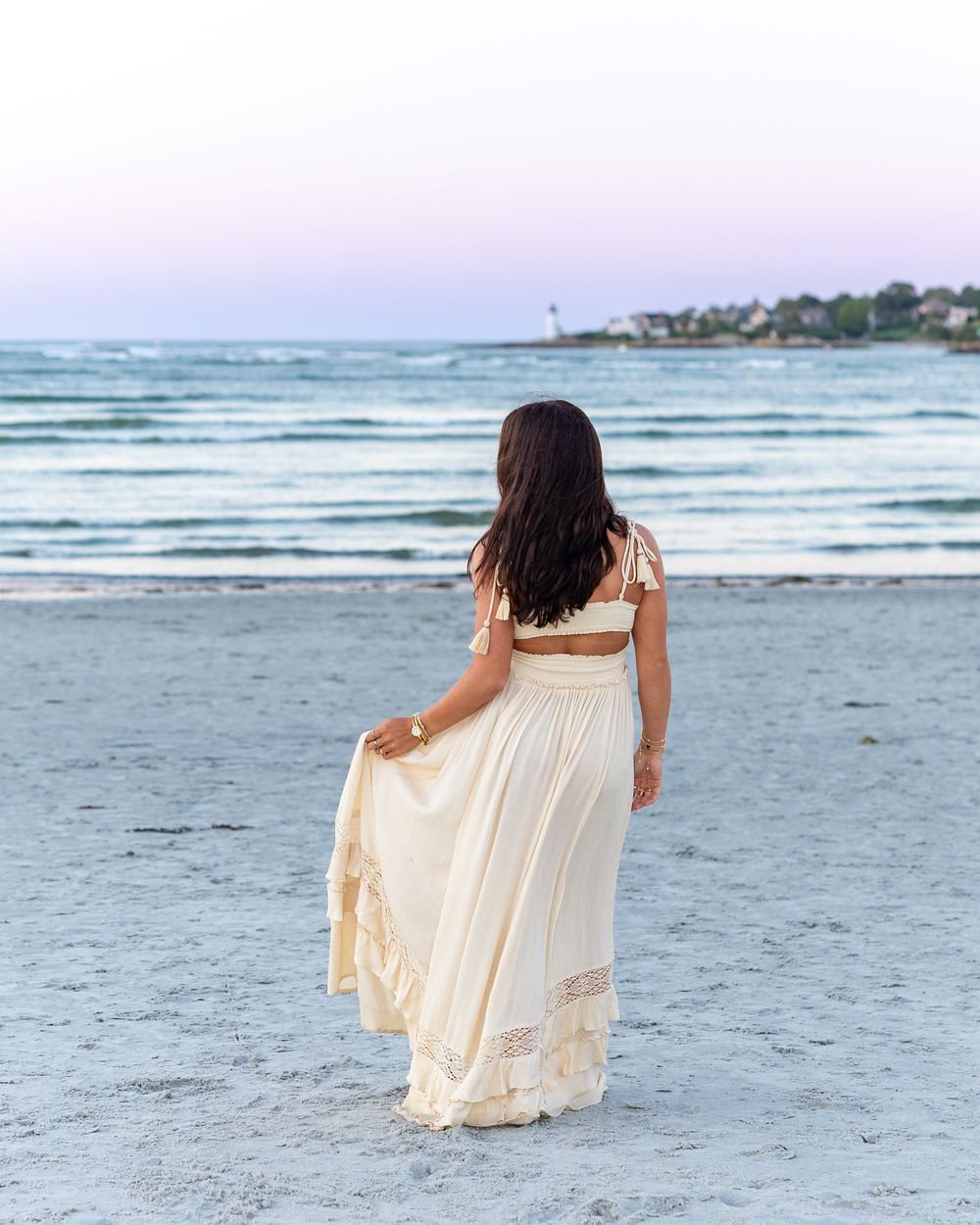 High school senior cream lace maxi dress stands near ocean at Wingaersheek Beach in Gloucester, MA for yearbook portrait session at sunset.