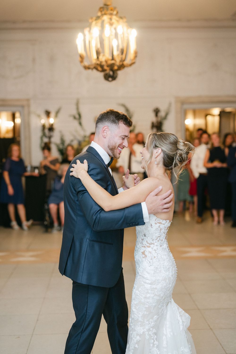 Bride and groom share their first dance under a golden chandelier at an elegant wedding reception.