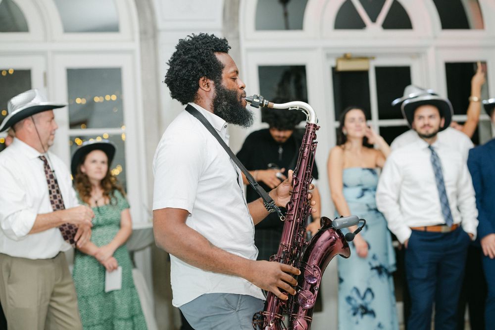Saxophonist performing live at an outdoor wedding reception with guests dancing in the background.
