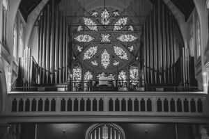 Black and white photo of a church organ with ornate rose window stained glass backdrop inside a grand cathedral.